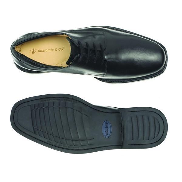 A top-down view of the two Anatomic Leme Black Oxford Shoes, with one shoe positioned upside down to display the synthetic sole. The image provides a clear view of the shoe's sole pattern and the detailed construction of the heel and toe areas.