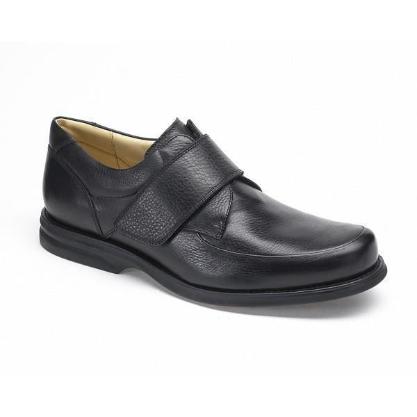 The shoe is angled to highlight the elegant curve from the toe to the heel. The burnished black leather finish gives the shoe a vintage yet sophisticated look, while the Velcro strap provides modern functionality.