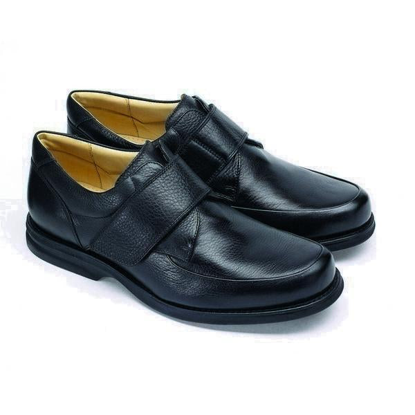 The shoe is angled to highlight the elegant curve from the toe to the heel. The burnished black leather finish gives the shoe a vintage yet sophisticated look, while the Velcro strap provides modern functionality.