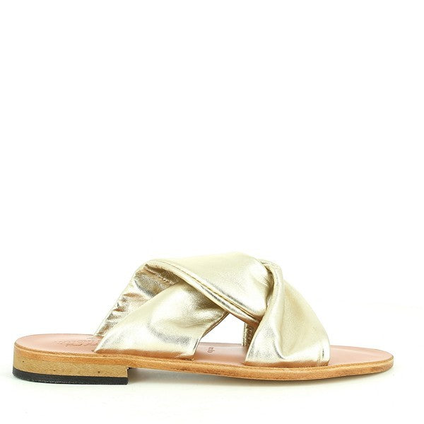 The Antichi Romani 068 Platino Gold Knot Slides feature a gleaming gold leather upper with an elegant knot detail at the front. The slides showcase a round toe and a sleek leather sole, highlighted by their 2 cm heel-platform for a subtle lift. The luxurious gold finish contrasts beautifully against a neutral background, emphasizing the slides' sophisticated craftsmanship and Italian heritage. The image captures the refined details and high-quality materials of these women’s shoes.