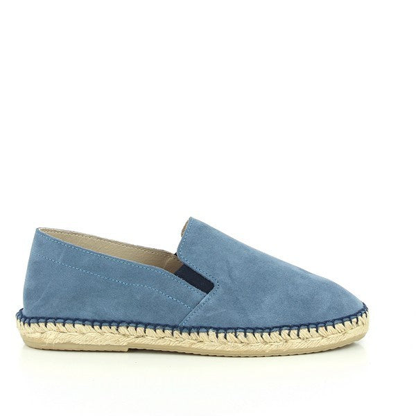 The photo features a pair of Calzanor 1980 Jeans Blue Espadrilles. These espadrilles have a soft blue leather upper with a subtle, distressed finish, adding a rustic charm. The hand-stitched jute sole has a natural look and texture, showcasing the eco-friendly materials. The shoes have a rounded toe and a low 2 cm platform that provides both comfort and a slight lift. The interior lining is also leather, ensuring a breathable fit.