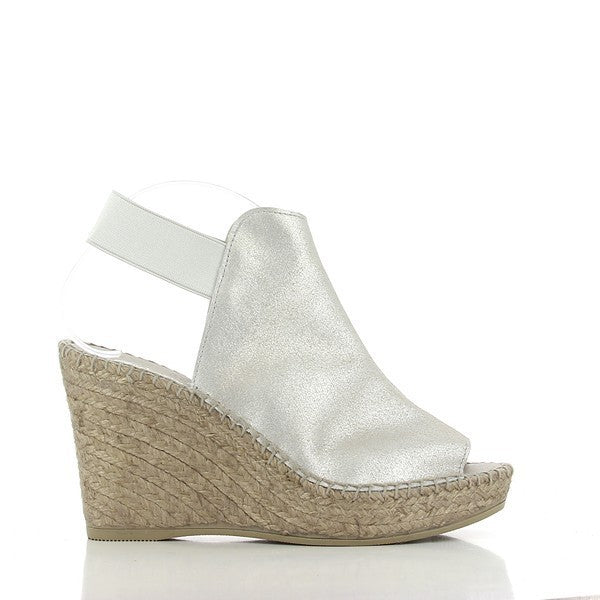 A close-up shot of the Calzanor 2127 Silver Slingback Espadrilles showcases their elegant design and craftsmanship. The upper features a sleek silver leather finish that shimmers in the light, highlighting the quality of the material. The soft leather lining is subtly visible, ensuring comfort and style. The espadrilles are set against a natural background, emphasizing their eco-friendly jute sole, which is designed for flexibility and breathability. 