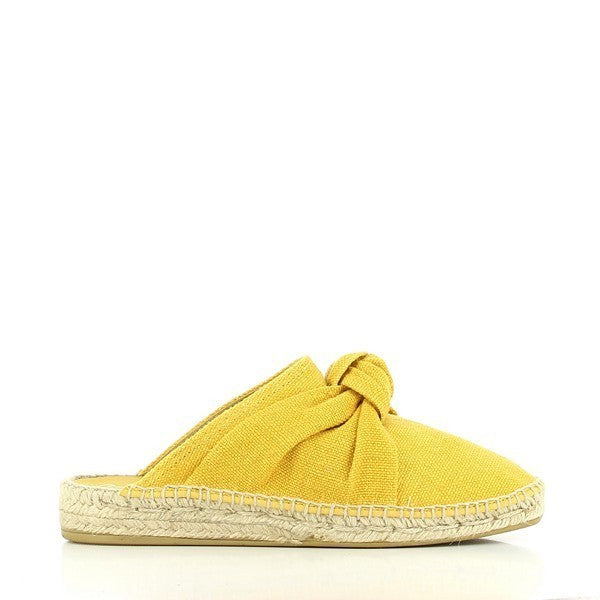 A pair of Calzanor 2147 Yellow Slide Espadrilles is elegantly positioned against a soft, neutral backdrop. The bright yellow leather upper catches the light, showcasing its smooth texture and vibrant hue. A charming front decorative knot adds a playful accent, enhancing the espadrilles' stylish appeal. The round toe shape contributes to a classic look, while the natural jute sole peeks out, highlighting its breathable and flexible qualities. 